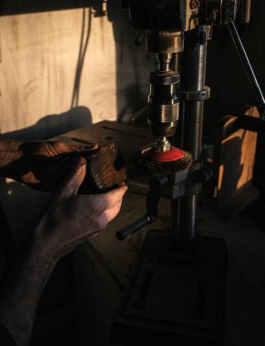 Close-up of hands holding a wooden object being polished with a power tool. The warm lighting adds to the focus on craftsmanship, precision, and the detailed woodwork process. clipart