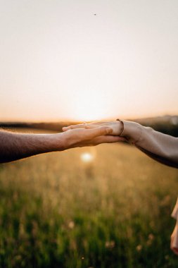 Gün batımında açık bir alanda birbirine uzanan iki el, sakin bir bağlantı anını yakalıyor, doğa ve sükunet. Sıcak ışık, duygusal ve huzurlu atmosferi güçlendirir..