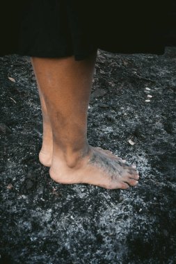 Bare feet covered in ash and dirt rest on a scorched, ashy surface, symbolizing resilience and connection to the earth. The image conveys themes of survival, hardship, and the raw elements of life. clipart