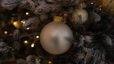 Altın ve bronz mücevherlerin yakın çekimleri bir Noel ağacını sıcak peri ışıklarıyla süsleyerek neşeli ve rahat bir tatil atmosferi yaratıyor..