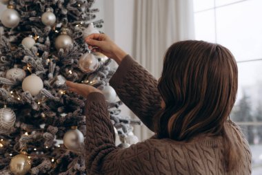 Güzel dekore edilmiş bir Noel ağacına süs takan, sıcak ve şenlikli bir atmosfer yaratan, rahat örgü ören bir kadının dikiz görüntüsü..