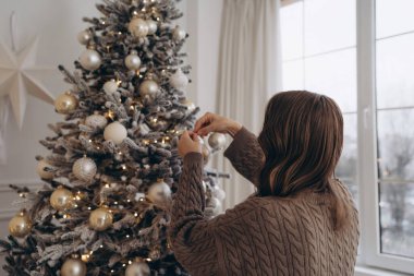 Güzel dekore edilmiş bir Noel ağacına süs takan, sıcak ve şenlikli bir atmosfer yaratan, rahat örgü ören bir kadının dikiz görüntüsü..