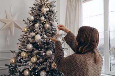 Güzel dekore edilmiş bir Noel ağacına süs takan, sıcak ve şenlikli bir atmosfer yaratan, rahat örgü ören bir kadının dikiz görüntüsü..