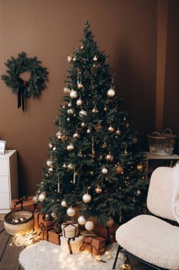 Altın ve bronz süslemeler, peri ışıkları ve çam kozalaklarıyla süslenmiş güzel dekore edilmiş bir Noel ağacı. Paketlenmiş hediyeler altında oturur, sıcak tatil atmosferini tamamlar..
