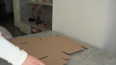 Bir kadın elinin dokulu bir yüzey üzerinde Kraft kartonu monte ettiğini gösteren bir video. Süreç, küçük işletmeler veya ekolojik bilinç sahipleri için sürdürülebilir ambalaj çözümlerini vurguluyor
