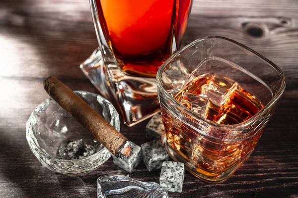 A gA glass of scotch whiskey with ice and a cigar on a wooden table. Food photo.
