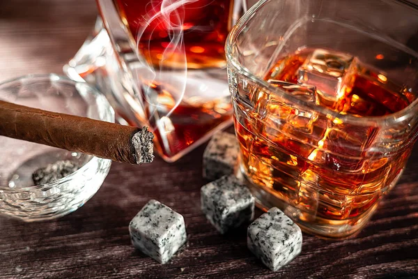 A gA glass of scotch whiskey with ice and a cigar on a wooden table close-up. Food photo.