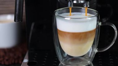 Sütlü cam bardağa doldurulan kahvenin yakın plan çekimi, otomatik kahve makinesiyle kapuçino yapmak. Kahve..