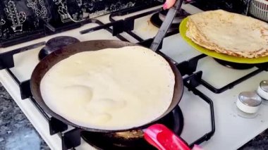 Bir kadın tavaya krep hamuru döker. Krepler tavada kızarır. Ev yapımı Rus krepleri pişirme süreci. Krepten duman yükselir. Yemek pişirme.