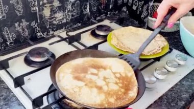 Kızartma sırasında siyah bir tavada krep pişirme işlemi, krep silikon bir spatulayla çevrilir. Yemek pişirme.