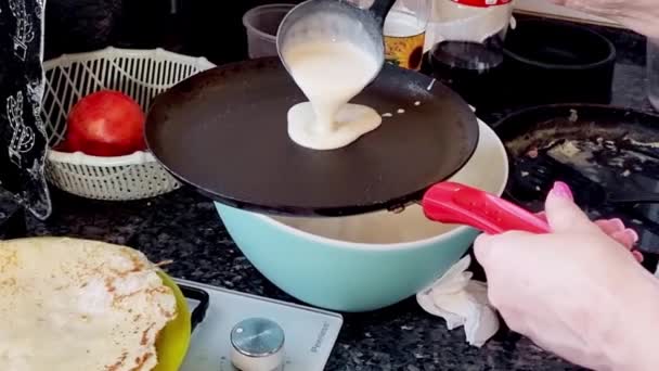 一个女人把煎饼面糊倒在一个煎锅里 煎饼放在锅里煎 烤自制俄罗斯煎饼的过程 煎饼里冒出做饭的烟 — 图库视频影像
