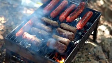 Açık havada ızgarada ızgara sosis yakın plan. Tabaklar mangalda pişiyor. Izgarayı ağız sulandırıcı sosislerle çeviriyor. Piknik ve kamp için yiyecek konsepti. B-B-Q.