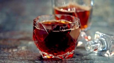 Buz küpü bir bardak viskinin içine düşer. Ağır çekim. Ağır çekimde, viski ahşap bir masaya sıçrar. Viski..