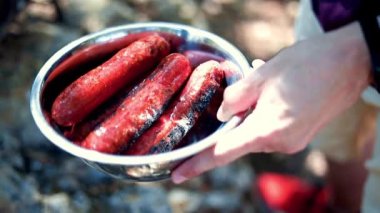 Kızarmış sosisler yakın planda metal bir kasede yatıyor. Tabaklar mangalda pişiyor. Piknik ve kamp için yiyecek konsepti. B-B-Q.