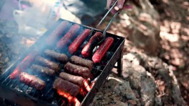 Izgara sosisler açık havada ızgarada kızartılıyor. Tabaklar mangalda pişiyor. Izgarayı iştah açıcı sosislerle çeviriyor. piknik ve kamp yemeği konsepti. B-B-Q.