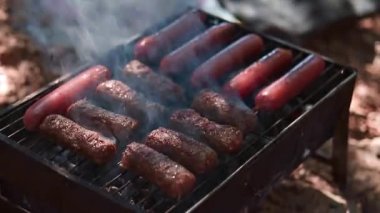 Izgara sosisler açık havada ızgarada kızartılıyor. Tabaklar mangalda pişiyor. Izgarayı iştah açıcı sosislerle çeviriyor. piknik ve kamp yemeği konsepti. B-B-Q.