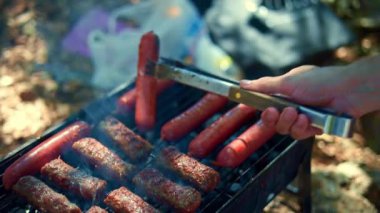Izgara sosisler açık havada ızgarada kızartılıyor. Tabaklar mangalda pişiyor. Izgarayı iştah açıcı sosislerle çeviriyor. piknik ve kamp yemeği konsepti. B-B-Q.