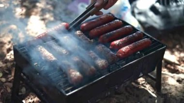 Izgara sosisler açık havada ızgarada kızartılıyor. Tabaklar mangalda pişiyor. Izgarayı iştah açıcı sosislerle çeviriyor. piknik ve kamp yemeği konsepti. B-B-Q.