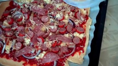 Bir ev hanımı mutfağında pizza hazırlıyor. Hamur, soğan, sosis, peynir ve sos serpiştirilmiş. Pizza..