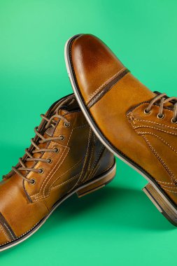 Yeşil arka planda bir çift kaliteli dana derisi bot. Dikey çekim. Erkek ayakkabısı fikirleri.