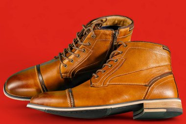 Kırmızı arka planda bir çift dana derisi bot. Yatay çekim. Erkek ayakkabısı fikirleri.