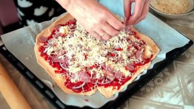 Bir ev hanımı mutfağında pizza hazırlıyor. Hamur, soğan, sosis, peynir ve sos serpiştirilmiş. Pizza..