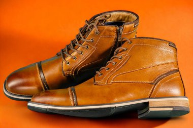 Turuncu arka planda bir çift dana derisi bot. Yatay çekim. Erkek ayakkabısı fikirleri.