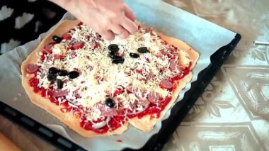 Bir ev hanımı mutfağında pizza hazırlıyor. Yuvarlak hamura soğan, sosis, peynir, zeytin ve sos serpilmiş. Pizza..