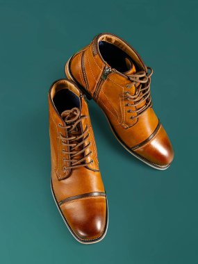 Yeşil arka planda bir çift kaliteli dana derisi bot. Dikey çekim. Erkek ayakkabısı fikirleri.