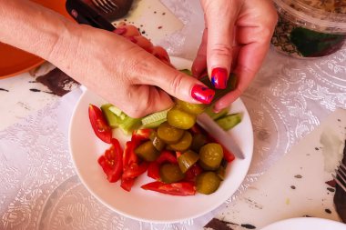 The girl cuts fresh and pickled vegetables into a plate. Vegetables. clipart