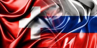 Rusya ve İsviçre 'nin ulusal bayrakları bir araya getirilip yan yana çırpınan bir pamuk zemin üzerinde yerleştirilmiştir..