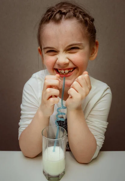 笑着坐在桌旁喝牛奶的小女孩 — 图库照片