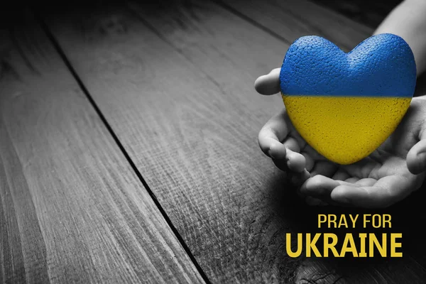 手はウクライナのために祈る言葉で暗い木製の背景に黄色と青の心を保持しています 助けと支援が必要です真実は勝つでしょう — ストック写真