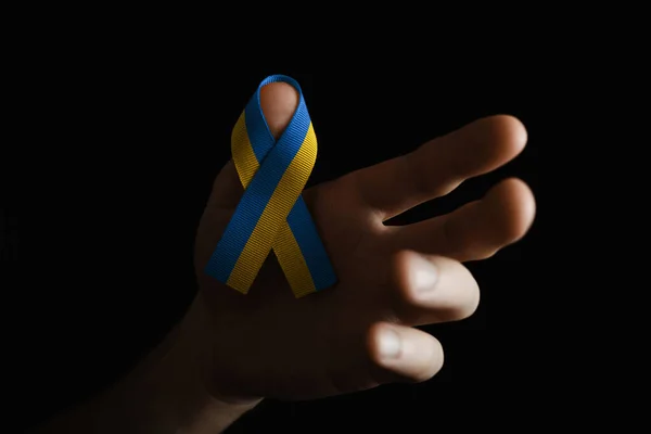 stock image wearing a yellow and blue ribbon on the finger, on dark background.. concept needs help and support, truth will win