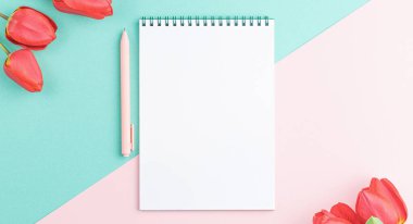 Open white spiral notebook with a pink pen and red tulip flowers on a two color background. Top view. Spring concept.