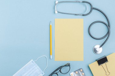 Medical equipment with stethoscope and note paper in doctor office on green background top view. Nurse desktop concept.