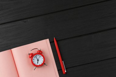 Pink open notebook with alarm clock and a pen on red isolated background top view.