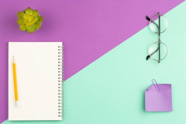 Kalem, gözlük, not kağıdı ve toka ile sarmal defteri aç ve iki renk arkaplan üzerinde yeşil yapraklar olan saksıya yerleştir. Üst manzara, düz uzanma.