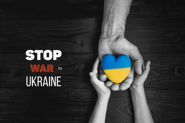 mans hand gives yellow and blue heart to hands of child. with words stop war in ukraine. black and white color. concept needs help and support, truth will win