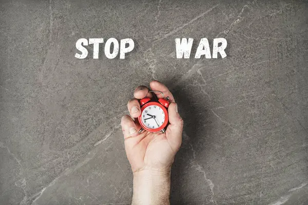 red alarm clock in hands on marble table with the inscription stop the war. time is running out you need to act. concept needs help and support, truth will win