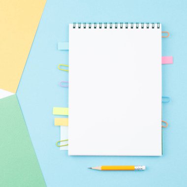 Kağıt ataçlarındaki yer imlerini içeren spiral bir defter aç, notlar için yapraklar, renkli kağıt geometrik şekillerdeki kalem arkaplan görünümü. Kırtasiye konsepti. Ofis araçları.