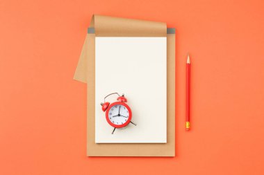 Beyaz sayfalı eskiz defteri, turuncu izole arka plan görünümlü kırmızı alarm saati ve kalem..
