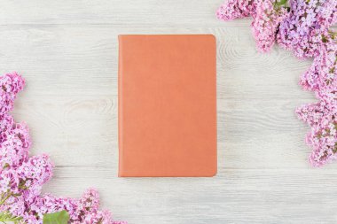 Beyaz ahşap bir arka planda el işi kitabı ve leylak çiçekleri. Üst görünüm.