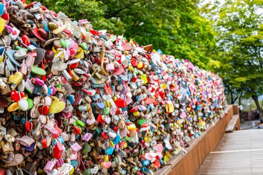 Editorial image showing a long wall of colorful heart-shaped love locks at N Seoul Tower in Seoul, South Korea, surrounded by green trees, representing the unity and lasting love of couples visiting the landmark