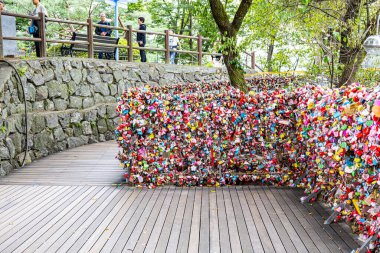 Editorial image showing a colorful section of love locks at N Seoul Tower in Seoul, South Korea, with visitors walking nearby, representing love, togetherness, and popular romantic tradition in Korea