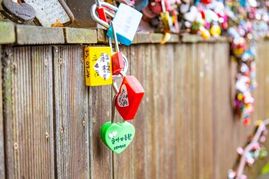 Güney Kore 'deki Namsan Seul Kulesi' nde demir parmaklıklara bağlanmış renkli kalp şeklinde asma kilitlerin yakın çekimi. Her kilitte, bu ünlü romantik topraklarda aşk ve daimi bağlılığı temsil eden el yazısıyla yazılmış mesajlar ve çiftlerin isimleri var.