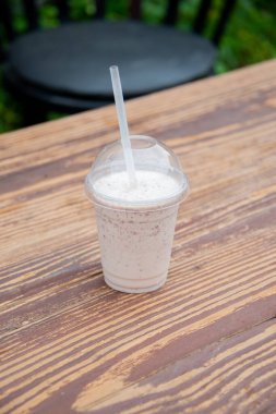 Plastik bardaktaki vanilyalı milkshake, tahta bir masada izole edilir..