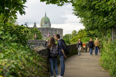 Arkadaki katedralle Corrib nehri boyunca yürüyen insanlar, Galway, İrlanda, Birleşik Krallık