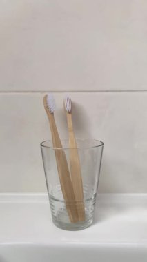 Bir dişi el cam bardaktan bambu bir diş fırçası alır. 4K dikey video. Banyo da biyolojik çözünebilir hijyen ürünleri var..