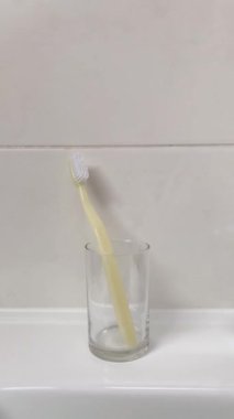 Bir kadının eli plastik bir diş fırçasını cam bardaktaki bambu bir fırçayla değiştirir. 4K dikey video. Banyo da biyolojik çözünebilir hijyen ürünleri var..
